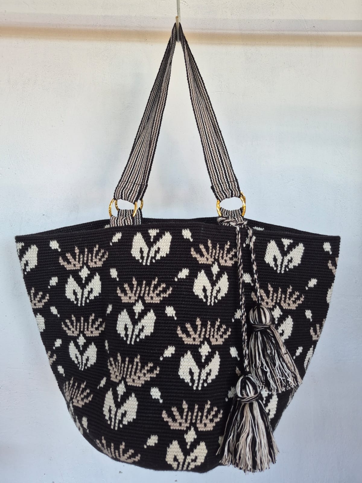 Totem Flor, bolso tejido a mano en crochet. Flores en marfil y arena sobre un fondo oscuro, con asas a rayas.